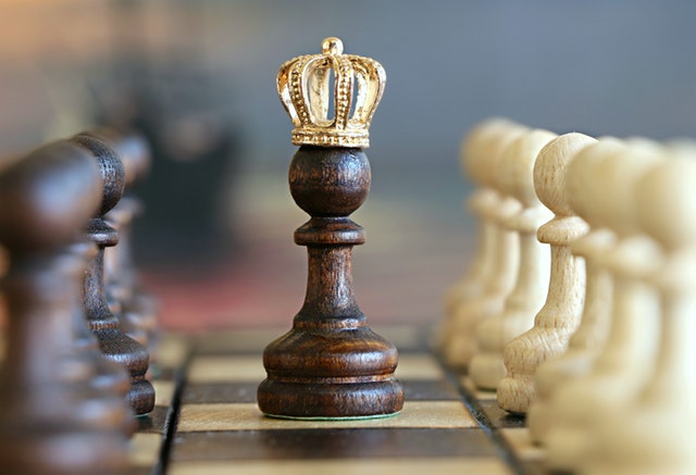 Hnedá šachová figúrka na šachovnici so zlatou korunou na hlave.jpg